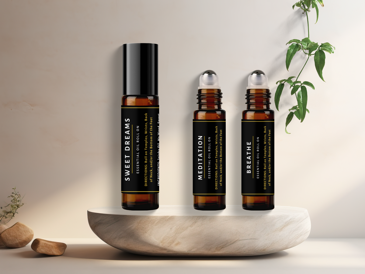 Three essential oil roller bottles labeled 'Sweet Dreams', 'Meditation', and 'Breathe' on a stone surface with a plant in the background.